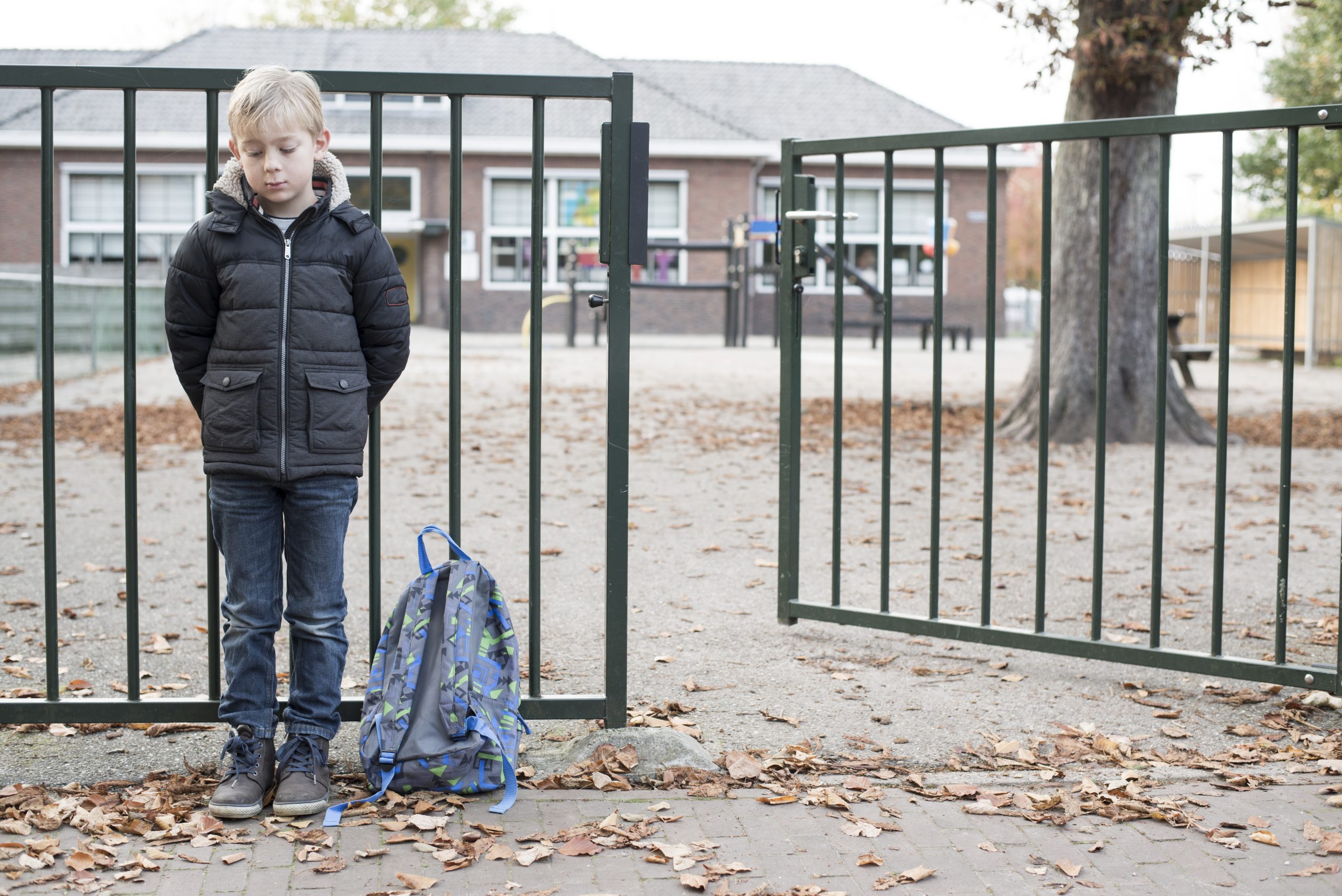 Boy standing outside a metal gate in front of a school