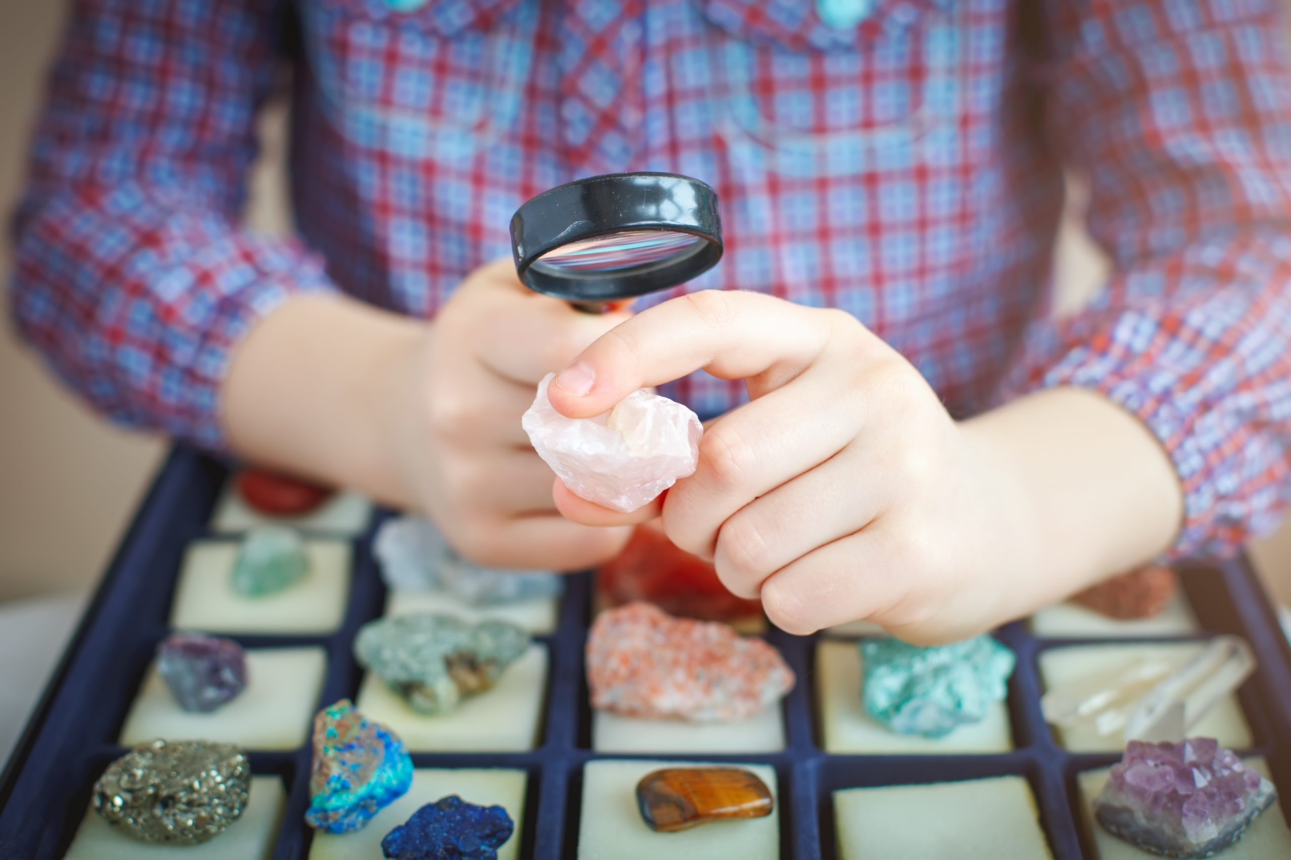 A Child Looks At His Collection Of Minerals with a Magnifying Glass